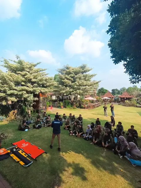 Peserta kegiatan duduk di tepi halaman hijau dengan pepohonan dan joglo di belakangnya.